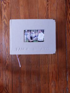 Detalle de la tapa del álbum de fotos de boda personalizado con lino gris claro y grabado en bajorrelieve “Paula & Axel”