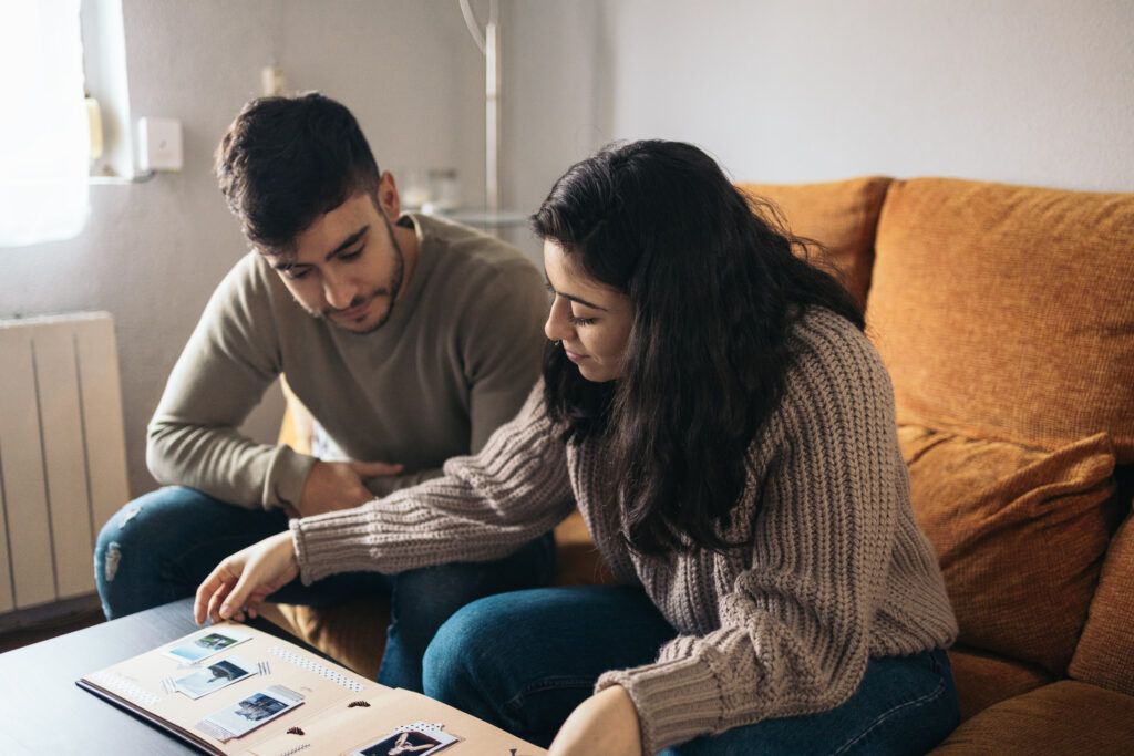 Pareja joven mirando un álbum de fotos con fotografías Polaroid de sus recuerdos de viaje en casa